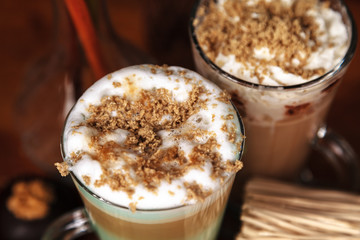 Coffee latte macchiato with mint syrup and whipped cream, sprinkled with chopped halva, in high transparent glasses, on a wooden table close-up, selective focus
