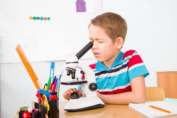 a seven-year-old boy at the table does the work, there is a microscope on the table