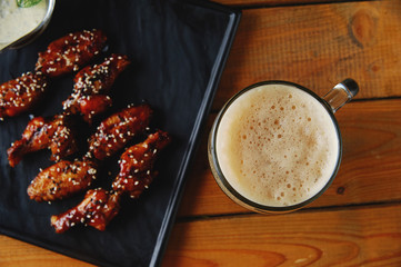 A glass of foamy dark beer with chicken wings. view from above