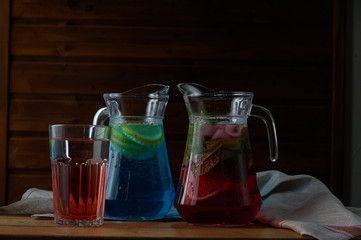 Two glass decanters, carafes, flagons with orange and berry lemonde on a wooden table with a black background