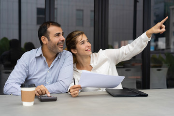 Cheerful business partners discussing real estate investment. Happy woman in formal shirt pointing...