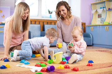 Babies toddlers crawling and having fun on floor in nursery. Mothers play with children in day care centre.