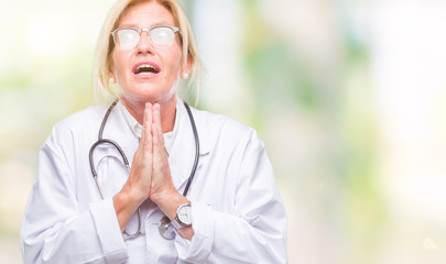 Middle age blonde doctor woman over isolated background begging and praying with hands together with hope expression on face very emotional and worried. Asking for forgiveness. Religion concept.