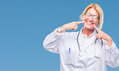 Middle age blonde doctor woman over isolated background smiling confident showing and pointing with fingers teeth and mouth. Health concept.