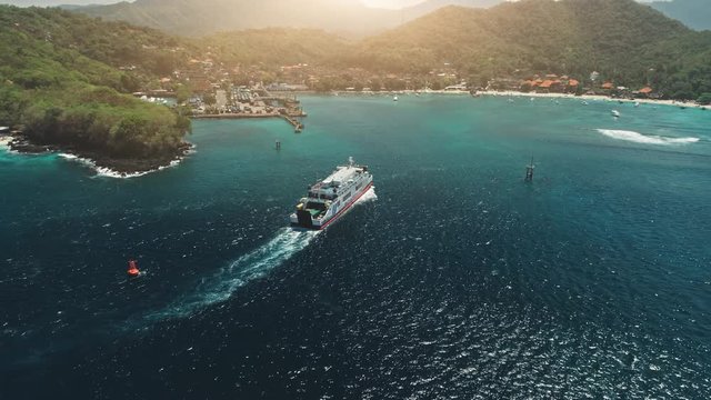 Aerial Drone View: Ferry sailing in harbor. Travel Vacation Recreation Paradise Tourism. Sunset mountain hills in background. Beautiful nature landscape in Tropical Bali Island. Cinematic filter. 4K