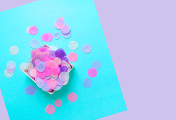Top view of box full of colorful confetti on pastel blue and violet background with copyspace.