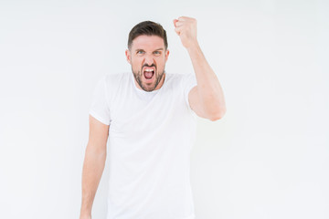 Fototapeta premium Young handsome man wearing casual white t-shirt over isolated background angry and mad raising fist frustrated and furious while shouting with anger. Rage and aggressive concept.
