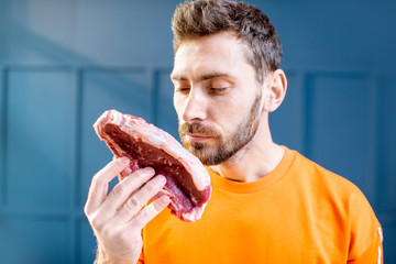 Conceptual portrait of a man dressed in bright sweater with raw meat steak on the blue background