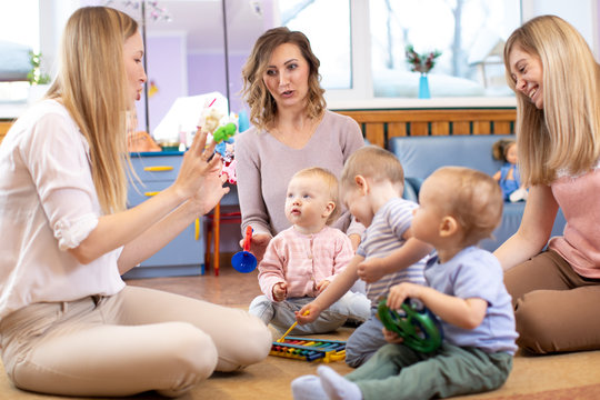 Mentor and 1 years old babies play with educational toys in kindergarten or daycare centre