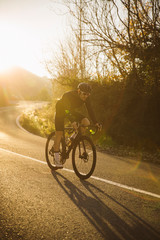 Professional road bicycle racer in action. Men cycling mountain road bike at sunset.