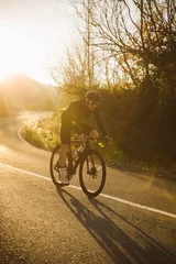 Gordijnen Professional road bicycle racer in action. Men cycling mountain road bike at sunset. © juananbarros