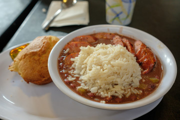 A bowl of beans and rice with sausage and a cornbread muffin on the side