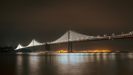 Fototapeta premium The Bay Bridge lit up at night with reflections on the Bay