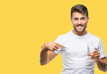 Young handsome man drinking glass of water over isolated background with surprise face pointing...