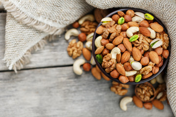 Wooden bowl with nuts on a wooden background, near a bag from burlap.