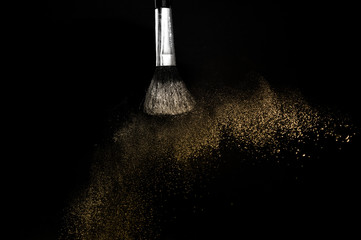 gold powder splash and brush for makeup artist or graphic design in black background, look like a luxury mood