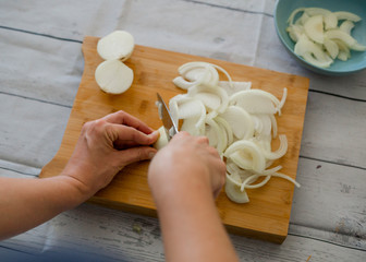 Obraz na płótnie Canvas Woman with knife cutting onion on wooden cutting board, close-up