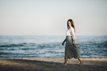 Marine female portrait. Attractive woman in green skirt walks along the shore before the sea
