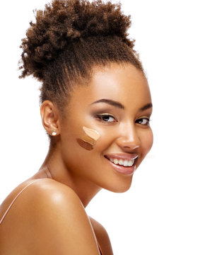 Beautiful smiling woman with tone cream lines on her face. Photo of african american girl with perfect makeup on white background. Skin care concept