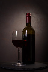 Wine bottle and glass with red wine on dark wooden background. Celebration concept. Copy space