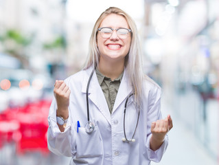 Young blonde doctor woman over isolated background very happy and excited doing winner gesture with arms raised, smiling and screaming for success. Celebration concept.