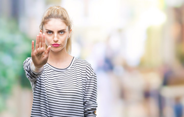 Young beautiful blonde woman wearing stripes sweater over isolated background doing stop sing with palm of the hand. Warning expression with negative and serious gesture on the face.