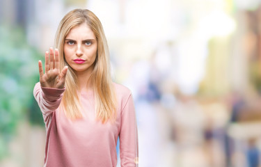 Young beautiful blonde woman wearing pink winter sweater over isolated background doing stop sing with palm of the hand. Warning expression with negative and serious gesture on the face.