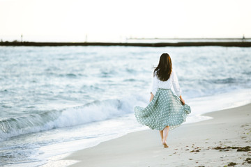 Marine female portrait. Attractive woman in green skirt walks along the shore before the sea