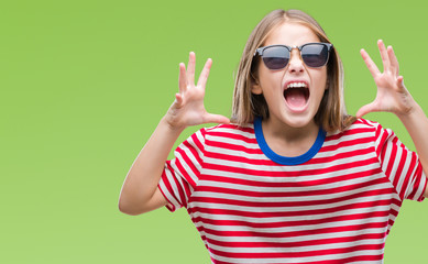 Young beautiful girl wearing sunglasses over isolated background crazy and mad shouting and yelling with aggressive expression and arms raised. Frustration concept.