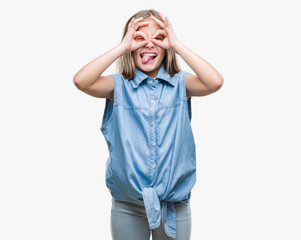 Young beautiful girl over isolated background doing ok gesture like binoculars sticking tongue out, eyes looking through fingers. Crazy expression.