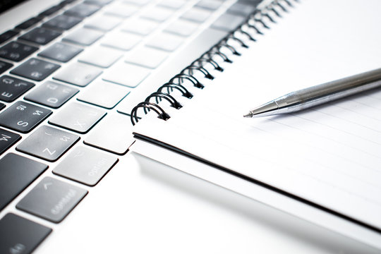 A close up photo of a pen placed on a notebook and computer.