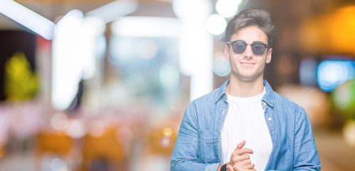 Fototapeta na wymiar Young handsome man wearing sunglasses over isolated background Hands together and fingers crossed smiling relaxed and cheerful. Success and optimistic