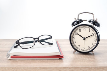 Concept Education or business : The glasses  put on the red book with black alarm clock on wooden table isolated on white background.