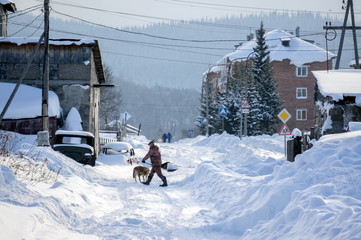 Man with a shovel cleans snow on the outskirts of the village on the background of residential...