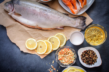 Kraft paper raw fish with lemon slices lies on a dark gray table top on a white plate. A variety of...