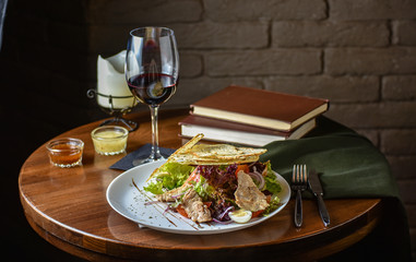 Fresh and tasty salad and red vine on the table. Food still life, home cooking recipe. Natural light, slightly toned image, dark black background with text area. Horizontal view.