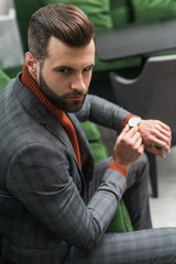 man in formal wear sitting on green sofa and adjusting watch on hand