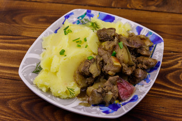 Mashed potatoes with stewed chicken liver with apple and onion on wooden table