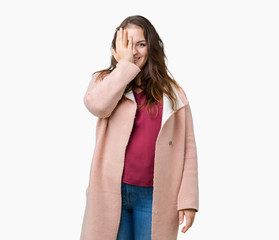 Beautiful plus size young woman wearing winter coat over isolated background covering one eye with hand with confident smile on face and surprise emotion.