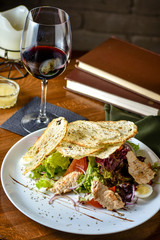 Fresh and tasty salad and red vine on the table. Food still life, home cooking recipe. Natural light, slightly toned image, dark black background with text area. Vertical view.