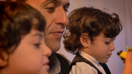 Close-up portrait of middle-aged arabic father in profile playing with his twin sons trifling with toys in living room.