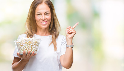 Middle age hispanic woman eating popcorn over isolated background very happy pointing with hand and finger to the side