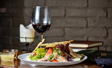 Fresh and tasty salad and red vine on the table. Food still life, home cooking recipe. Natural light, slightly toned image, dark black background with text area. Horizontal view.