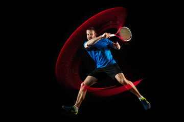 The one caucasian man playing tennis isolated on black background. Studio shot of fit young player at studio in motion or movement during sport game with led light trail - obrazy, fototapety, plakaty