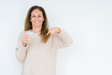 Middle age woman drinking glass of water isolated background with surprise face pointing finger to himself