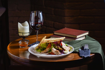 Fresh and tasty salad and red vine on the table. Food still life, home cooking recipe. Natural light, slightly toned image, dark black background with text area. Horizontal view.