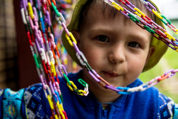 A smiling little boy in a yellow hat and blue sweater is looking through a colored chain.