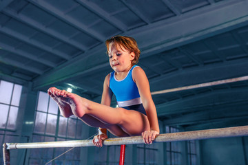 The beautiful little girl is engaged in sports gymnastics on a parallel bars at gym. The...