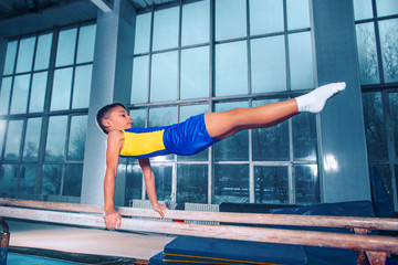 The little boy is engaged in sports gymnastics on a parallel bars at gym. The performance, sport,...