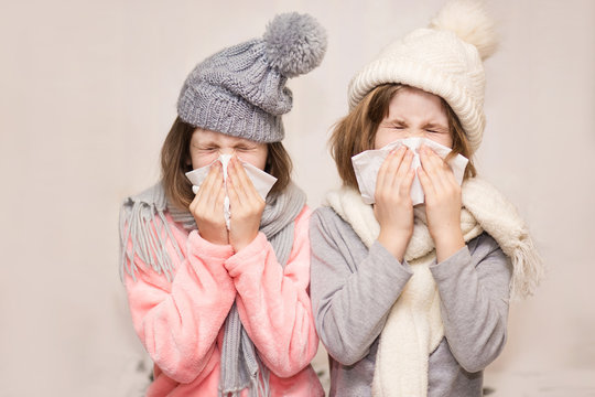Sick little sisters in funny hat blowing noses with napkins